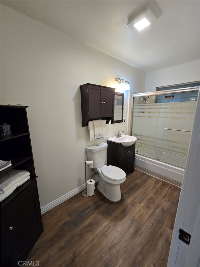 full bathroom with wood-type flooring, bath / shower combo with glass door, toilet, and vanity