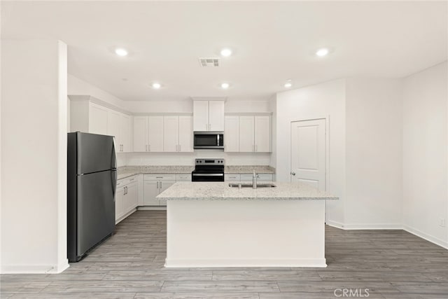 kitchen with sink, white cabinetry, stainless steel appliances, light stone countertops, and an island with sink