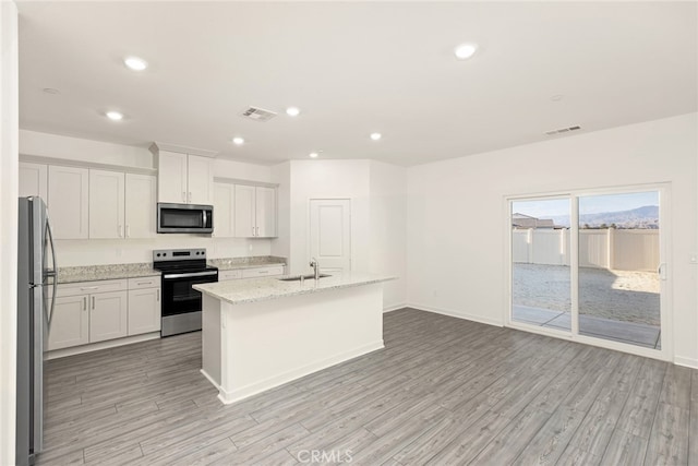 kitchen with light stone counters, a kitchen island with sink, stainless steel appliances, light hardwood / wood-style floors, and white cabinets