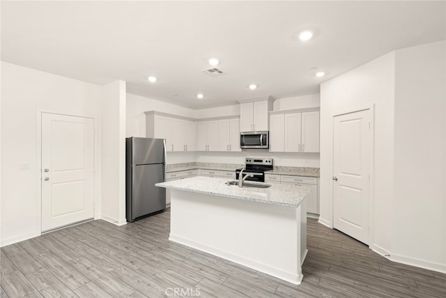 kitchen with white cabinetry, stainless steel appliances, light hardwood / wood-style floors, and a kitchen island with sink