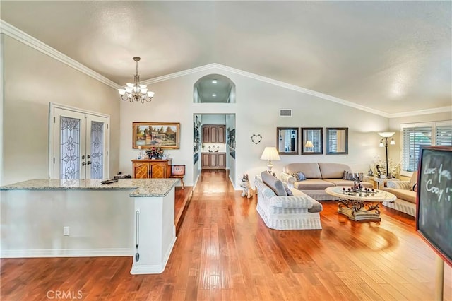 living room featuring vaulted ceiling, an inviting chandelier, crown molding, and light hardwood / wood-style flooring