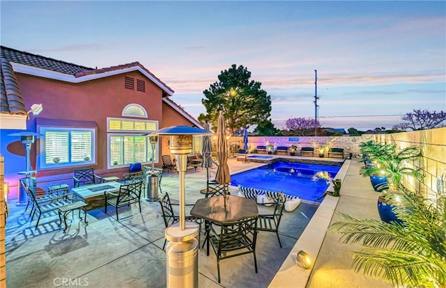 pool at dusk with a patio area and a fireplace