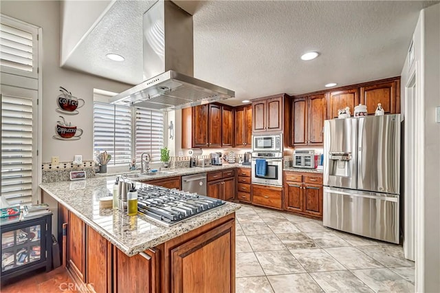 kitchen featuring kitchen peninsula, sink, stainless steel appliances, island range hood, and light stone counters