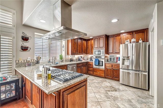 kitchen with light stone countertops, appliances with stainless steel finishes, island exhaust hood, sink, and kitchen peninsula