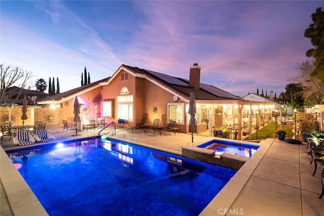 pool at dusk with an in ground hot tub and a patio