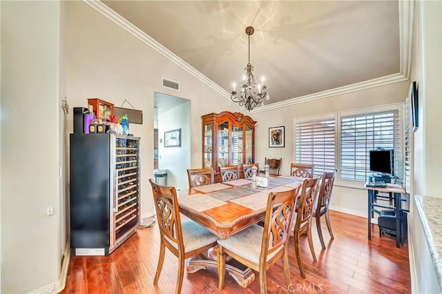 dining room featuring hardwood / wood-style flooring, beverage cooler, a notable chandelier, and vaulted ceiling