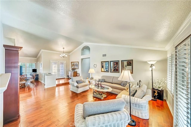 living room with lofted ceiling, wood-type flooring, an inviting chandelier, and ornamental molding