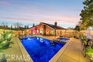 pool at dusk featuring a patio area and an in ground hot tub