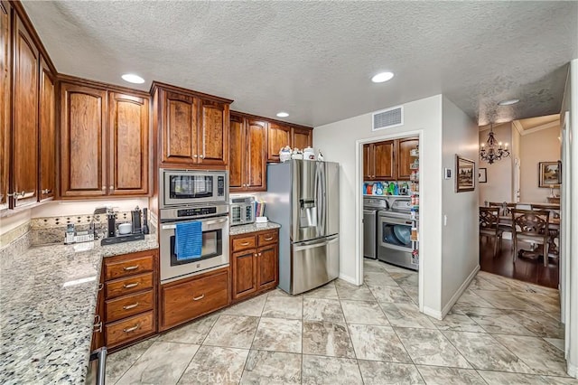 kitchen featuring light stone countertops, a textured ceiling, appliances with stainless steel finishes, washing machine and clothes dryer, and an inviting chandelier