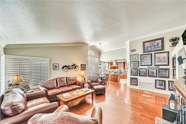 living room featuring lofted ceiling, crown molding, a textured ceiling, and light hardwood / wood-style floors