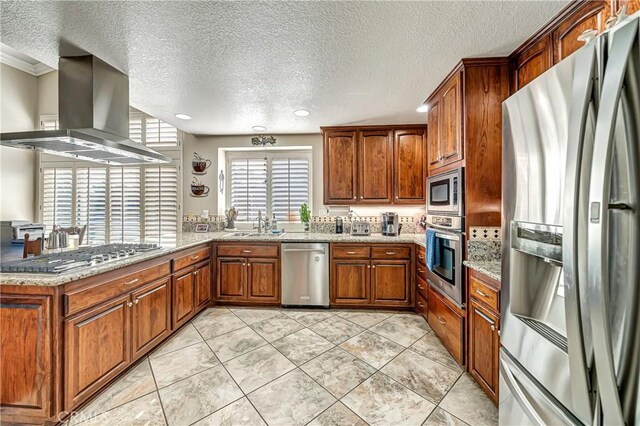 kitchen with island exhaust hood, stainless steel appliances, kitchen peninsula, and light stone countertops