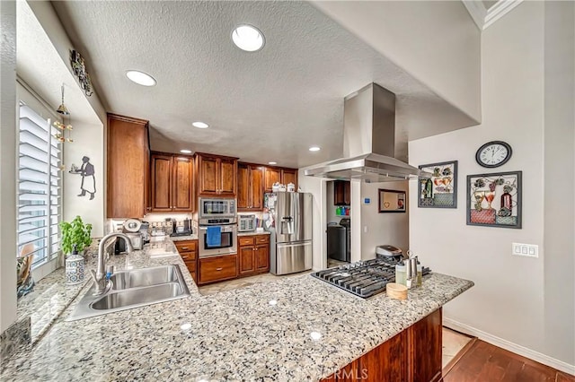 kitchen with kitchen peninsula, sink, island exhaust hood, light stone countertops, and appliances with stainless steel finishes