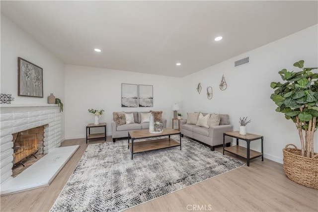 living area featuring recessed lighting, visible vents, a brick fireplace, wood finished floors, and baseboards