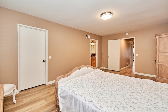 bedroom featuring connected bathroom and light hardwood / wood-style flooring