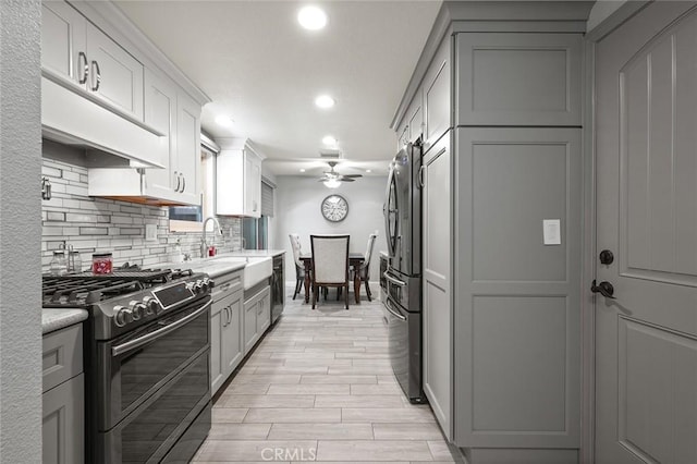 kitchen with decorative backsplash, double oven range, sink, ceiling fan, and gray cabinetry