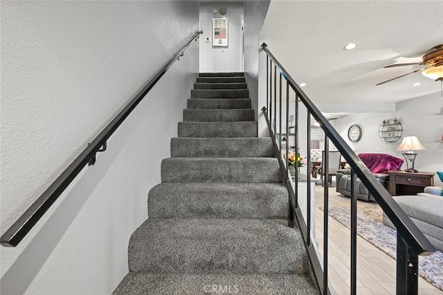 staircase with a textured ceiling, ceiling fan, and hardwood / wood-style flooring