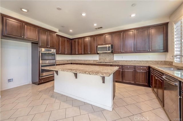 kitchen with stainless steel appliances, a kitchen breakfast bar, light stone countertops, a kitchen island, and sink