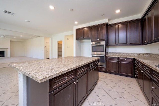 kitchen with stainless steel double oven, a fireplace, light tile patterned flooring, and a kitchen island