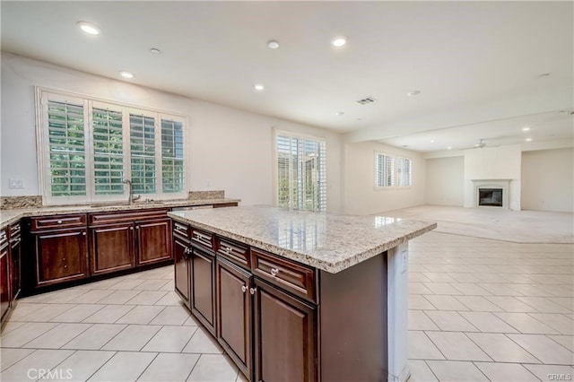 kitchen with light tile patterned floors, a center island, a fireplace, light stone countertops, and sink