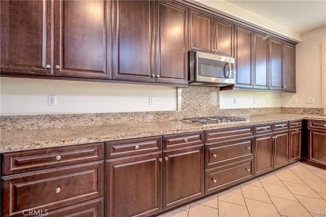 kitchen featuring light tile patterned flooring, appliances with stainless steel finishes, light stone counters, and dark brown cabinetry