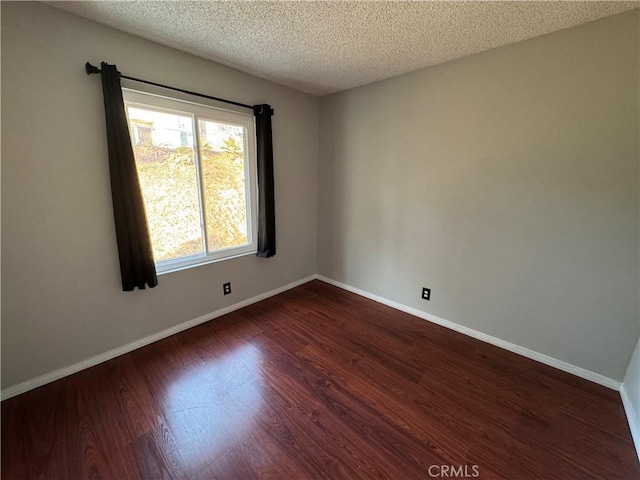 unfurnished room featuring a textured ceiling, dark wood finished floors, and baseboards