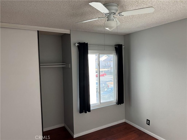 unfurnished bedroom featuring dark wood-style floors, a textured ceiling, baseboards, and a closet