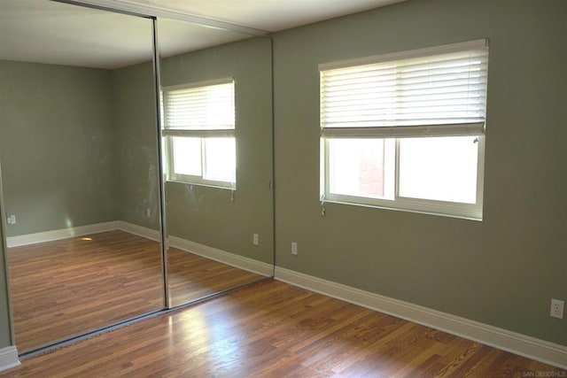 unfurnished bedroom with a closet, multiple windows, and hardwood / wood-style flooring