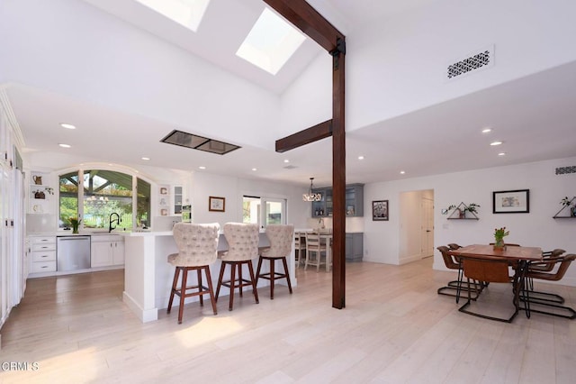 kitchen with a skylight, dishwasher, white cabinetry, and a center island