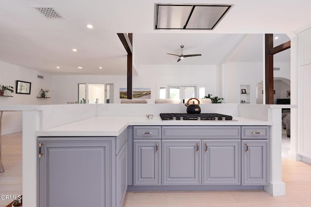 kitchen featuring ceiling fan, a kitchen island, gray cabinetry, gas stovetop, and light stone counters