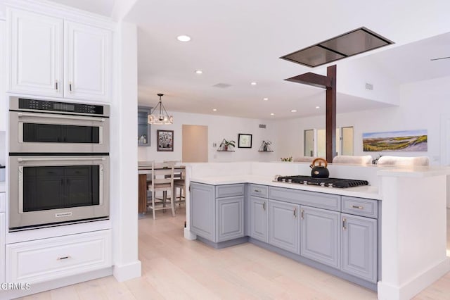 kitchen featuring pendant lighting, white cabinets, stainless steel appliances, light wood-type flooring, and gray cabinetry