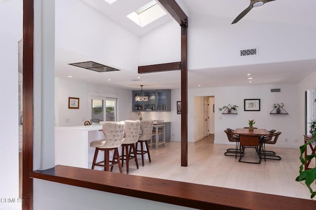 dining space with ceiling fan, light hardwood / wood-style flooring, a skylight, and high vaulted ceiling