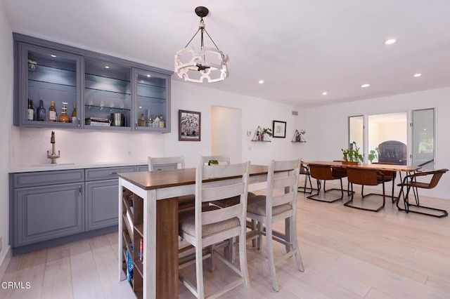 dining area with indoor wet bar, an inviting chandelier, and light wood-type flooring