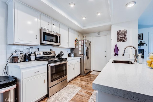 kitchen with appliances with stainless steel finishes, white cabinets, a tray ceiling, and sink