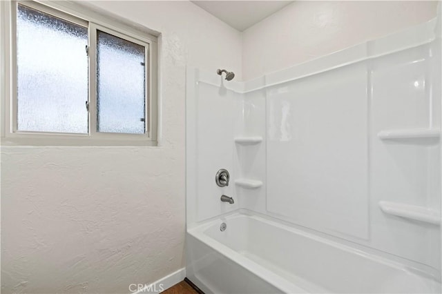 bathroom featuring baseboards, shower / washtub combination, and a textured wall