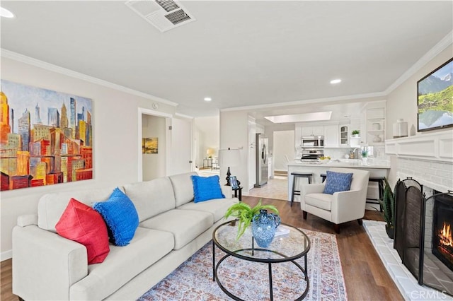 living room with wood finished floors, a fireplace, visible vents, and ornamental molding