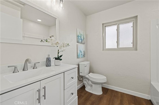 bathroom with toilet, a tub to relax in, wood finished floors, baseboards, and vanity