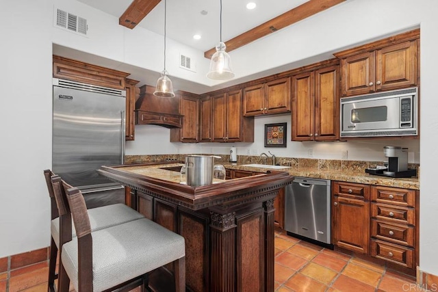 kitchen with premium range hood, sink, light stone counters, built in appliances, and an island with sink