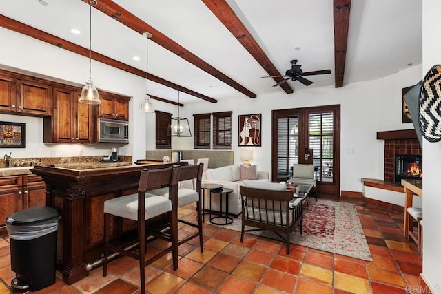 interior space featuring decorative light fixtures, stainless steel microwave, a tile fireplace, ceiling fan, and beam ceiling