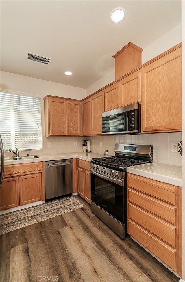 kitchen featuring dark hardwood / wood-style floors, tile countertops, sink, backsplash, and stainless steel appliances