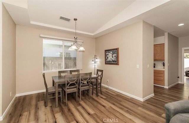 dining room with lofted ceiling, dark hardwood / wood-style flooring, a chandelier, and a tray ceiling