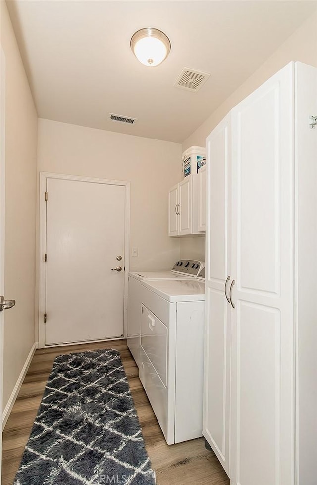 clothes washing area featuring cabinets, hardwood / wood-style floors, and washing machine and clothes dryer