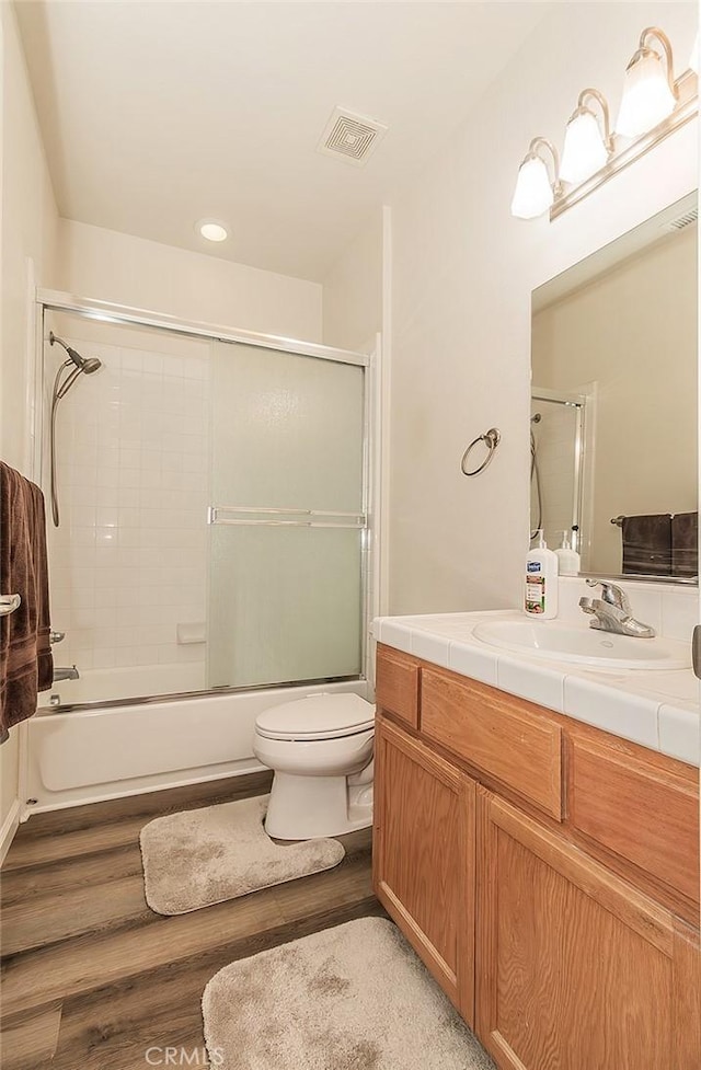 full bathroom featuring vanity, hardwood / wood-style flooring, bath / shower combo with glass door, and toilet