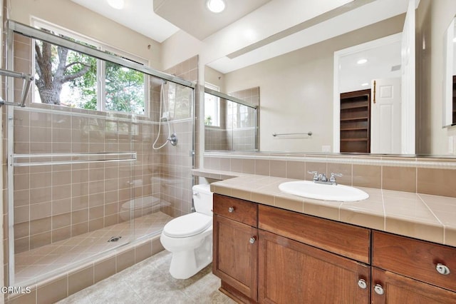 bathroom featuring toilet, tasteful backsplash, tile patterned flooring, walk in shower, and vanity