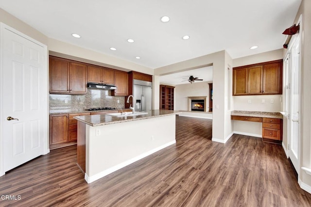 kitchen with appliances with stainless steel finishes, built in desk, dark wood-type flooring, an island with sink, and sink