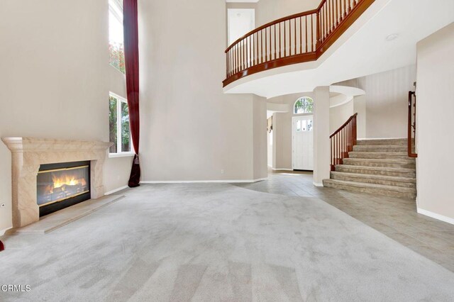 unfurnished living room with a premium fireplace, light carpet, and a high ceiling