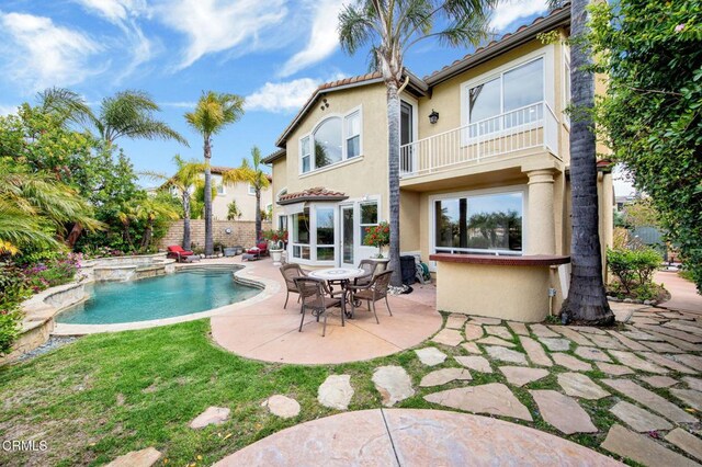 rear view of property with a balcony, a pool with hot tub, and a patio area