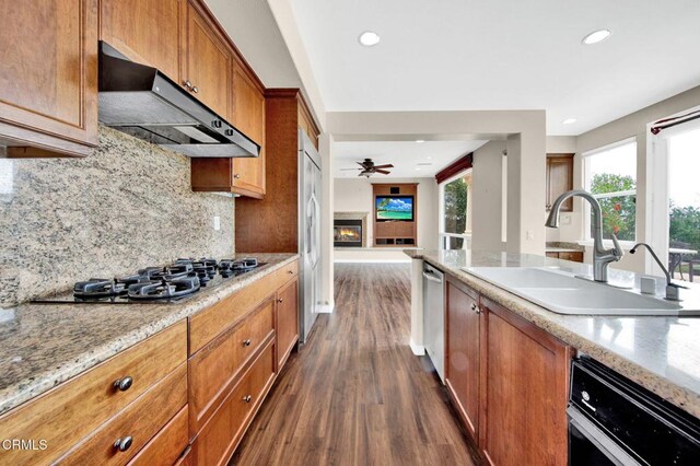 kitchen with appliances with stainless steel finishes, sink, dark hardwood / wood-style flooring, decorative backsplash, and light stone countertops