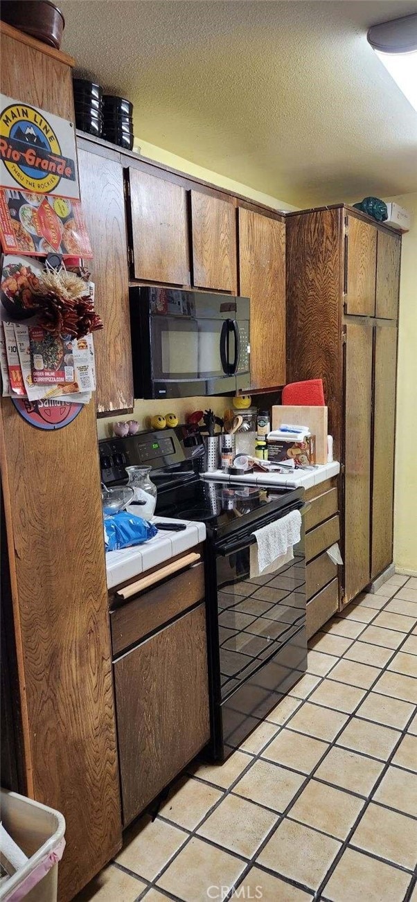 kitchen with a textured ceiling, light tile patterned floors, and black appliances