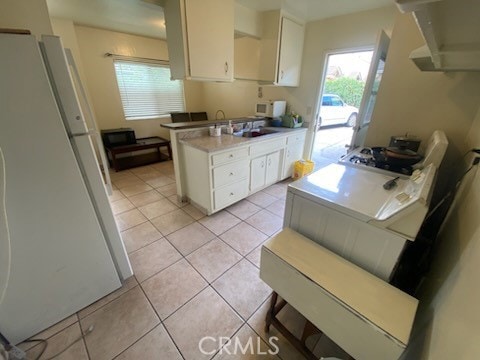 kitchen with light tile patterned floors, sink, white refrigerator, and white cabinetry