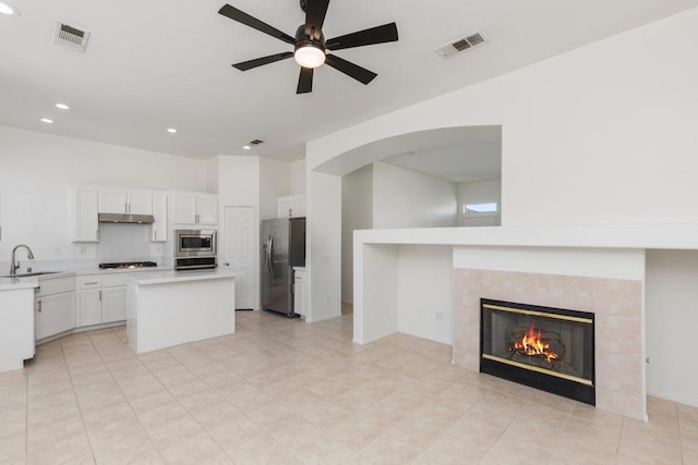 kitchen with white cabinets, a kitchen island, stainless steel appliances, ceiling fan, and a tile fireplace